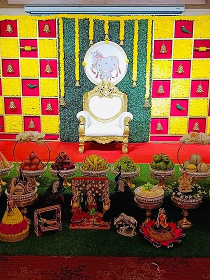 A classic Seemantham backdrop with a checkerboard of yellow marigolds and red fabric. The design is accented with small bells and parrot motifs, with a central elephant painting for good luck.