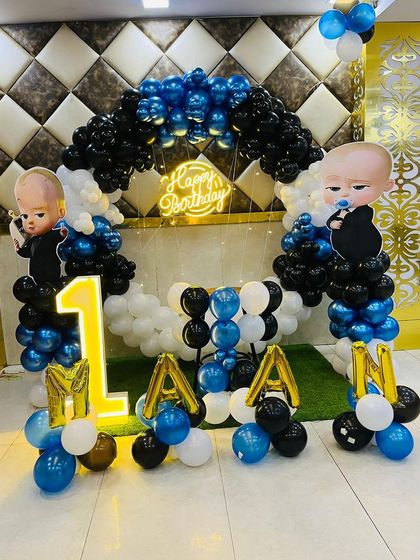 This is a duplicate of ID 30, 95, 208, 248, 253. A classic Boss Baby theme for a first birthday. This setup includes a balloon arch in blue, black, and white, character cutouts, a 'Happy Birthday' neon sign, and a light-up number '1'.