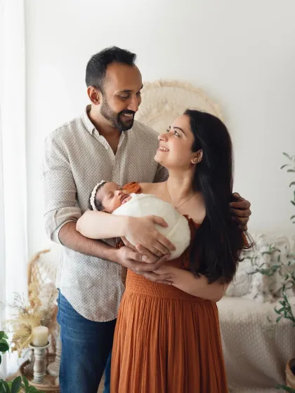 A happy family of three with their newborn baby in a relaxed studio setting. The parents' joyful expressions show their love for their new arrival.