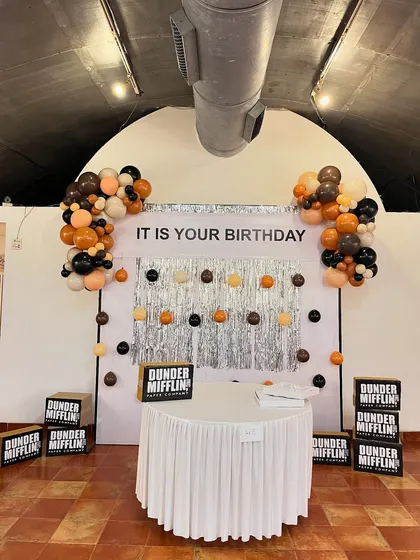 A wider shot of the main photo booth area for 'The Office' party. The setup captures the slightly awkward yet charming aesthetic of a Dunder Mifflin office party, complete with a drab color scheme and a metallic fringe curtain.