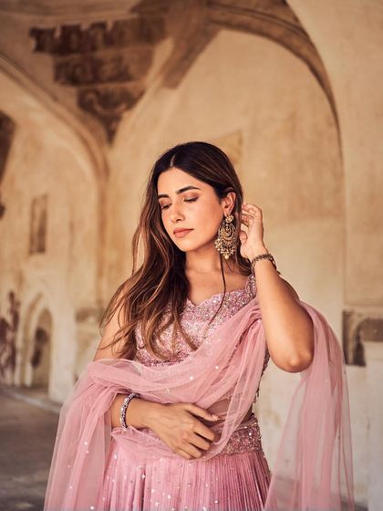 A soft and romantic portrait in a beautiful architectural setting. The natural light and the model's gentle pose perfectly complement the delicate, sequined pink lehenga.