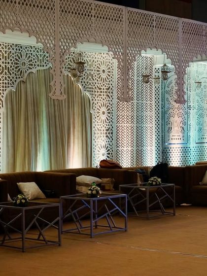 A cozy lounge area with brown sofas and a backdrop of white jali screens, creating an intimate and stylish space for guests.