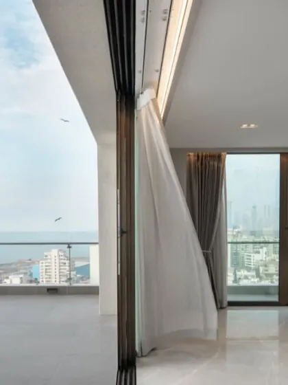 A moment of pause in a sea-facing penthouse. The design prioritizes the view, with floor-to-ceiling glass and an uncluttered layout that creates a seamless transition from the living space to the open sky and water.