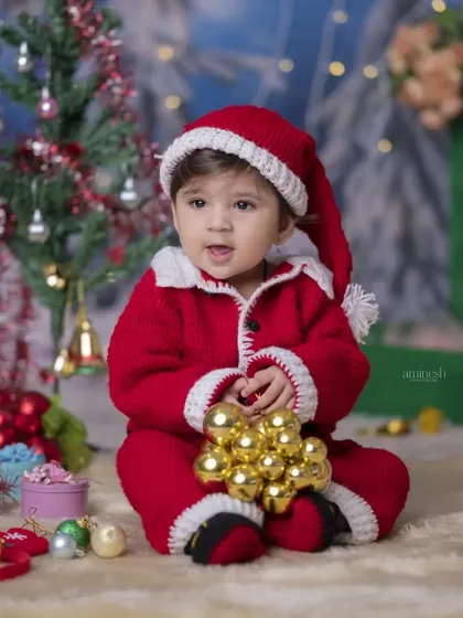 This little Santa is surrounded by golden ornaments and Christmas toys. The detailed setup and the baby's curious expression make for a heartwarming holiday photo.