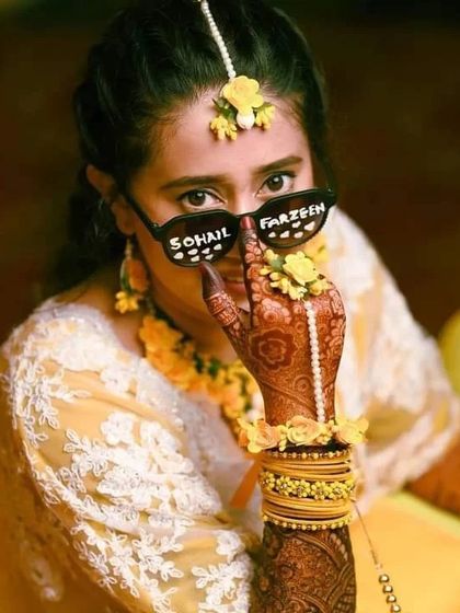 A quirky and fun photo of a bride with personalized sunglasses, her mehndi-adorned hand playfully covering her face.