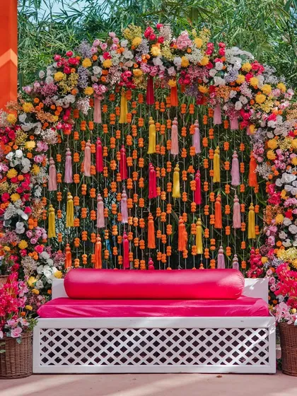 A colorful Mehendi seating area, with a floral arch backdrop and a fuschia pink sofa, perfect for the bride.