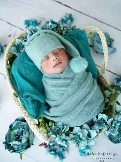 A beautiful composition with a baby in a teal pom-pom hat, surrounded by a bed of matching blue flowers.