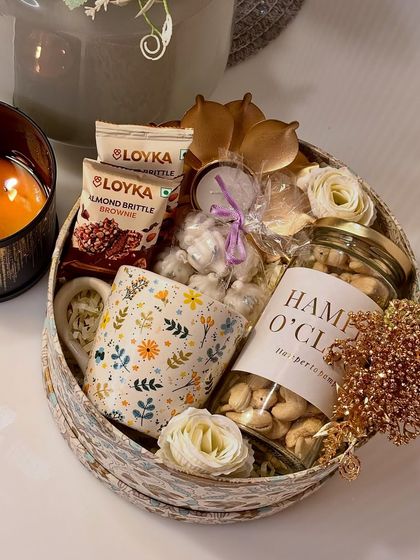 A cozy and comforting Diwali gift, this round festive box includes a printed coffee mug, a jar of premium cashews, a beautiful brass lotus diya, and other sweet treats. It's the perfect companion for a quiet, festive evening.
