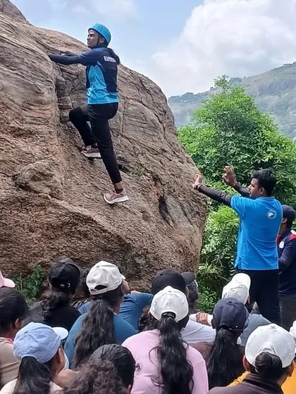 Learning from the best, right on the rock. An instructor demonstrates a fundamental bouldering technique to a group of new climbers at our Ramanagara camp, emphasizing hands-on learning and safety.
