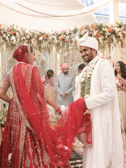 A beautiful moment between the bride and groom during the ceremony. The bride's classic red lehenga stands out beautifully against the soft, pastel decor of the mandap.