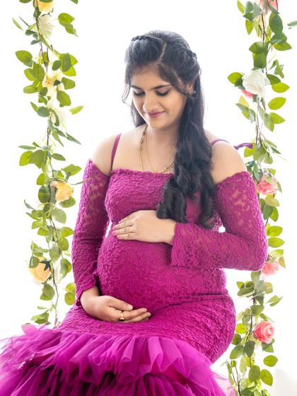 A dreamy solo portrait of a mom-to-be on a floral swing, dressed in a vibrant magenta lace and tulle gown.