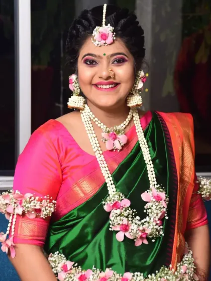A close-up of the smiling mom-to-be, showing the details of her maang tikka, jhumkas, and layered floral necklace.