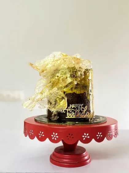 The full view of the Belgian Chocolate and dark toffee cake, standing on a bright red cake stand that makes the gold accents pop.