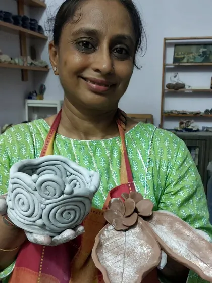 This talented student is showing off her beautiful creations from our workshop. She made a lovely bowl with a swirl pattern and a leaf-shaped dish. It's so rewarding to guide students and see them create things they are proud of.