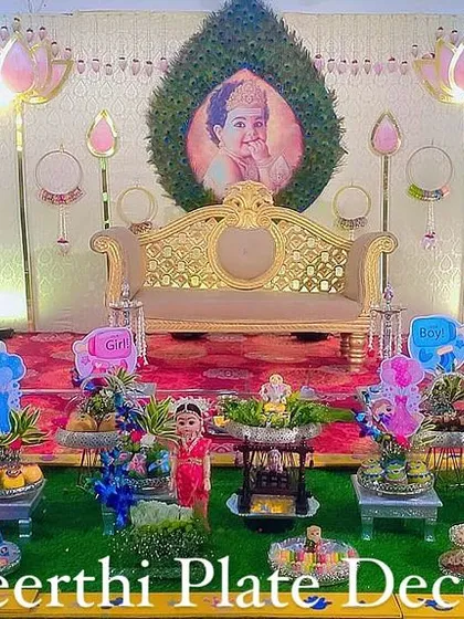 A beautiful baby shower setup with a lotus-themed backdrop and a personalized baby photo. The platter decorations are designed to match the pink and blue color scheme.