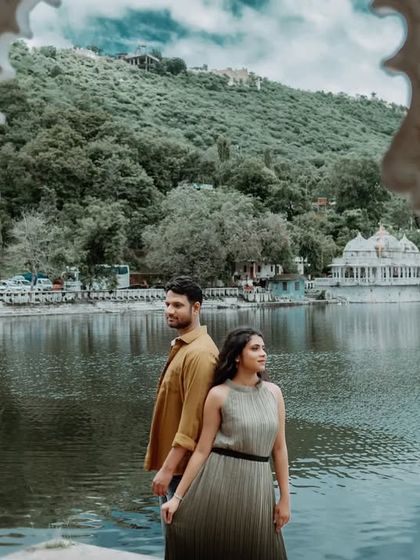 A beautifully framed shot of the couple through white pillars, with the serene lake and hills of Udaipur in the background. This composition adds depth and an artistic touch.