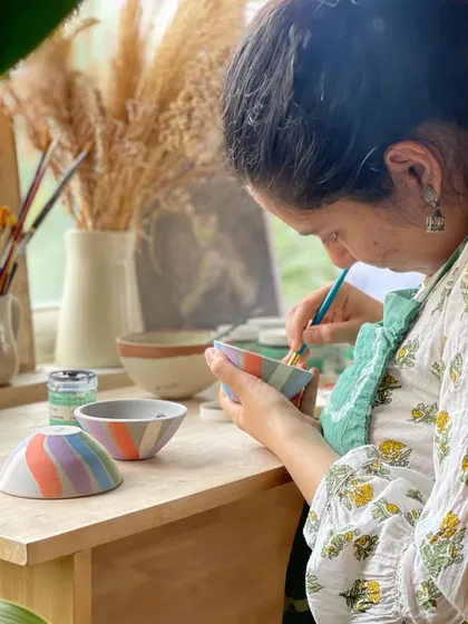 A student carefully paints colorful underglaze onto a set of small bowls, adding a personal and artistic touch to her creations.