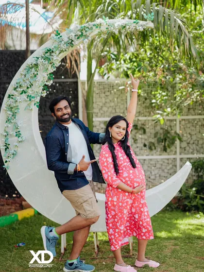 A playful and happy couple's portrait with a large crescent moon prop in a garden.