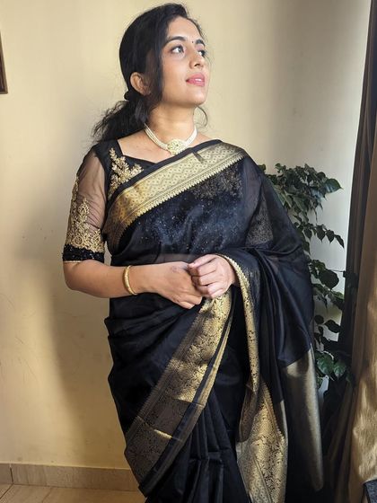 A full look of the black Kora Organza saree. It's styled with an embroidered blouse, showing how you can dress it up for a party or wedding reception.