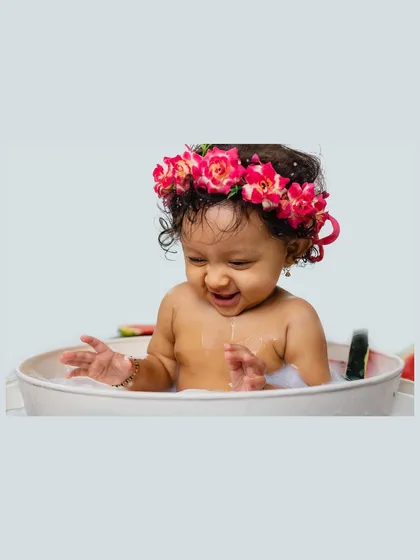 A candid shot of a baby girl splashing and smiling in her watermelon milk bath. This image captures a moment of pure, unscripted joy.