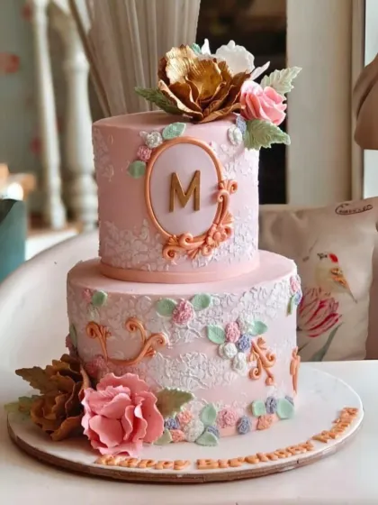 A vintage-inspired two-tier cake in soft pink, featuring intricate white lace piping and a monogrammed cameo.