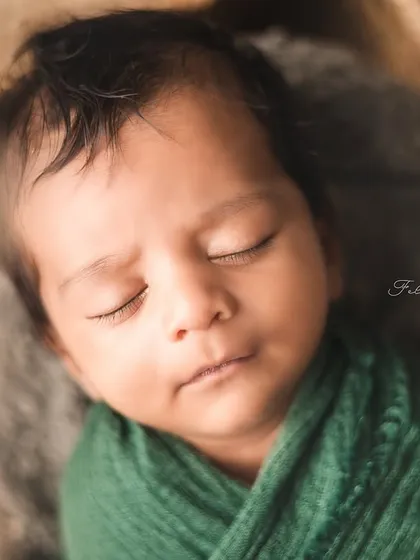 A sweet newborn rests in a rustic basket, wrapped in a cozy green swaddle. The natural textures and warm tones create a comforting and organic feel.