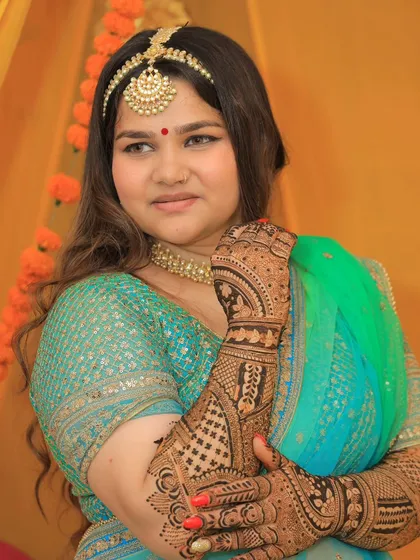 A beautiful portrait of a bride on her mehendi day, adorned with intricate henna. The design complements her traditional attire perfectly.