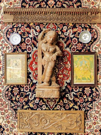 A celebration of human creativity. This wall features a hand-carved statue, antique paintings, and decorative plates, all arranged on a rich Persian carpet to tell a story of cultural legacy.