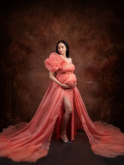 A serene and elegant pose in a beautiful peach gown. The soft lighting and classic backdrop create a timeless and graceful maternity portrait that feels like a classic painting.