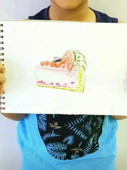 A student proudly shows off their drawing of a slice of cheesecake.