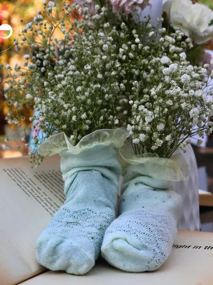 A creative centerpiece using baby socks as a vase for baby's breath, placed on an open book to tie into the literary theme.
