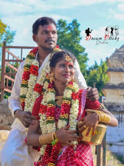 A beautifully composed outdoor shot of the couple near a temple structure. The bride is holding a traditional vessel, and the sunlight catches her happy expression, creating a timeless portrait.