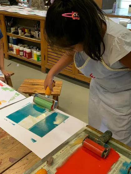 A young printmaker carefully rolls ink over her plate, ensuring an even coating before pressing it onto paper.