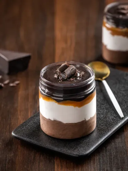 A close-up of a layered chocolate and caramel jar dessert, with a focus on the glossy top layer and distinct sections.