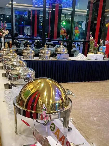 A vibrant and professional buffet setup for 100 guests in Noida. The combination of classic silverware and a bold, golden main chafing dish creates a striking focal point.