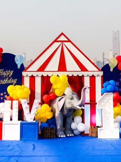 A classic circus stage setup against a city skyline, featuring a big top tent, a decorative ferris wheel, and personalized marquee letters.