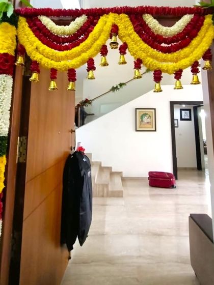 A door decoration for a housewarming using flower garlands with hanging bells. The yellow and red flowers create a festive and auspicious look.