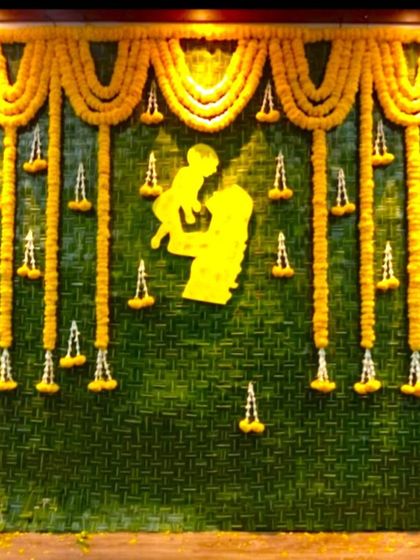 A traditional baby shower backdrop made of woven coconut leaves and marigold garlands. A cutout of a mother and child is placed in the center.
