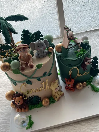 A pair of jungle-themed cakes for a first birthday. Both cakes feature handcrafted animal toppers and lush green details, perfect for a big celebration.