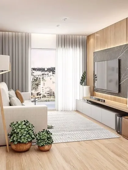A cozy and modern living room with a light wood floor and a TV unit set against a dark marble panel. The large window provides ample natural light.