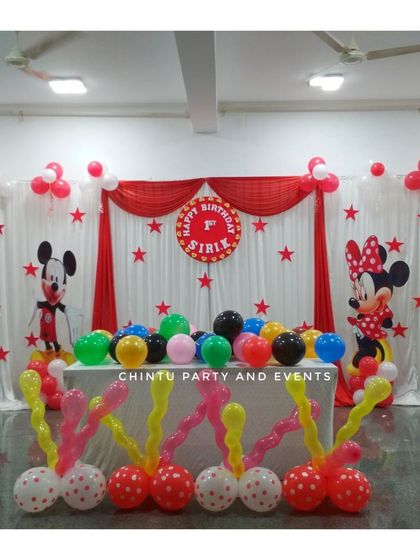 A Mickey and Minnie Mouse themed birthday stage. The classic red, white, and black color scheme is used for the drapes and balloon pillars.