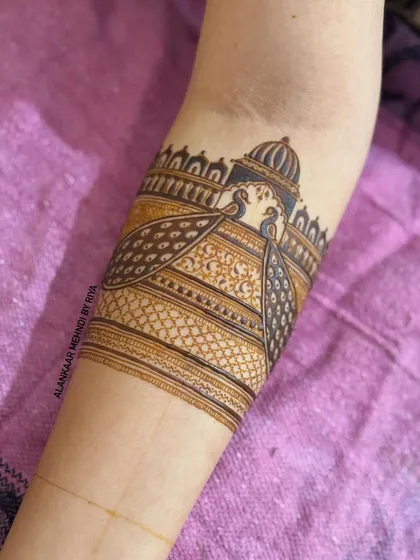An arm band featuring two peacocks against a palace, with their tails forming an intricate pattern.