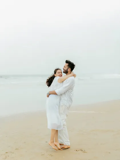 A candid shot of the couple sharing a laugh in a warm embrace on the beach.