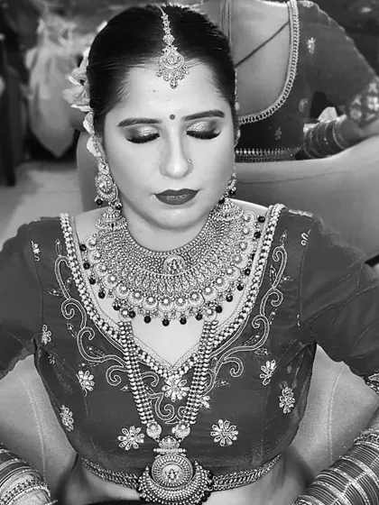 A classic black and white bridal portrait. The contrast highlights the detailed embroidery on her blouse, her heavy jewelry, and the flawless application of her makeup.