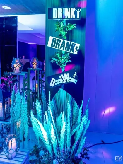 A fun corner at the bar area with signs that say 'Drinky Dranky Drunk'. This playful detail, combined with pampas grass and lanterns, adds personality and humor to the party.