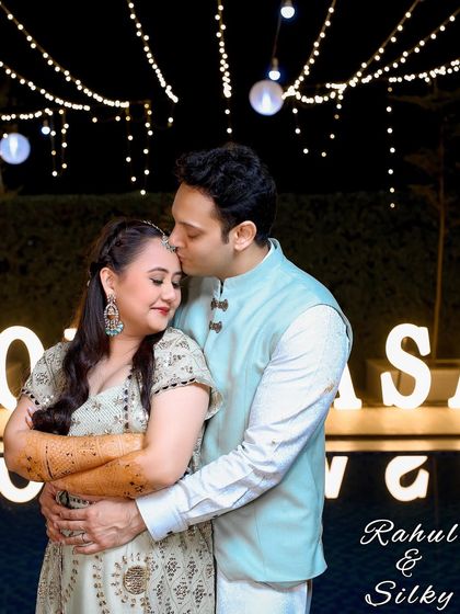 A sweet forehead kiss under a canopy of fairy lights. This photo captures the warmth and intimacy of an evening celebration.