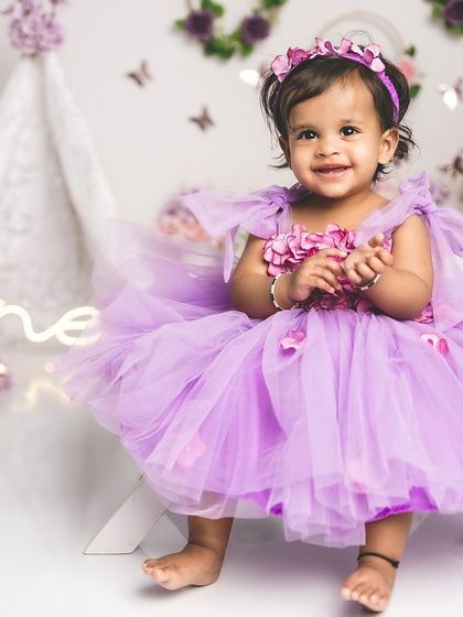 A beautiful, smiling one-year-old girl in a purple dress, ready to celebrate her special day.