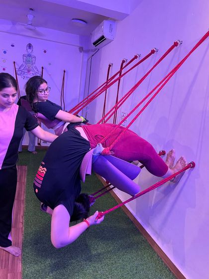 Guiding a student through a complex, inverted backbend using the wall ropes. This requires immense trust and strength.