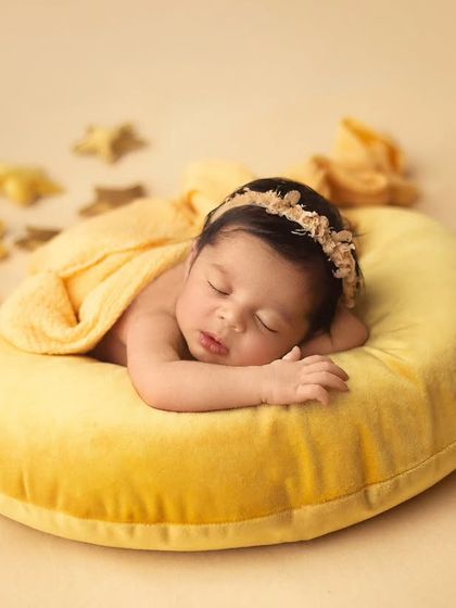 Another dreamy celestial setup, with the baby nestled on a soft yellow prop. The scattered stars add a touch of whimsy to this peaceful portrait.