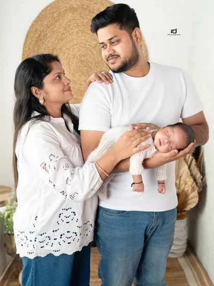 A look of love and protection. The parents gaze at their newborn, held securely in dad's arms, in a bright and airy studio setting.